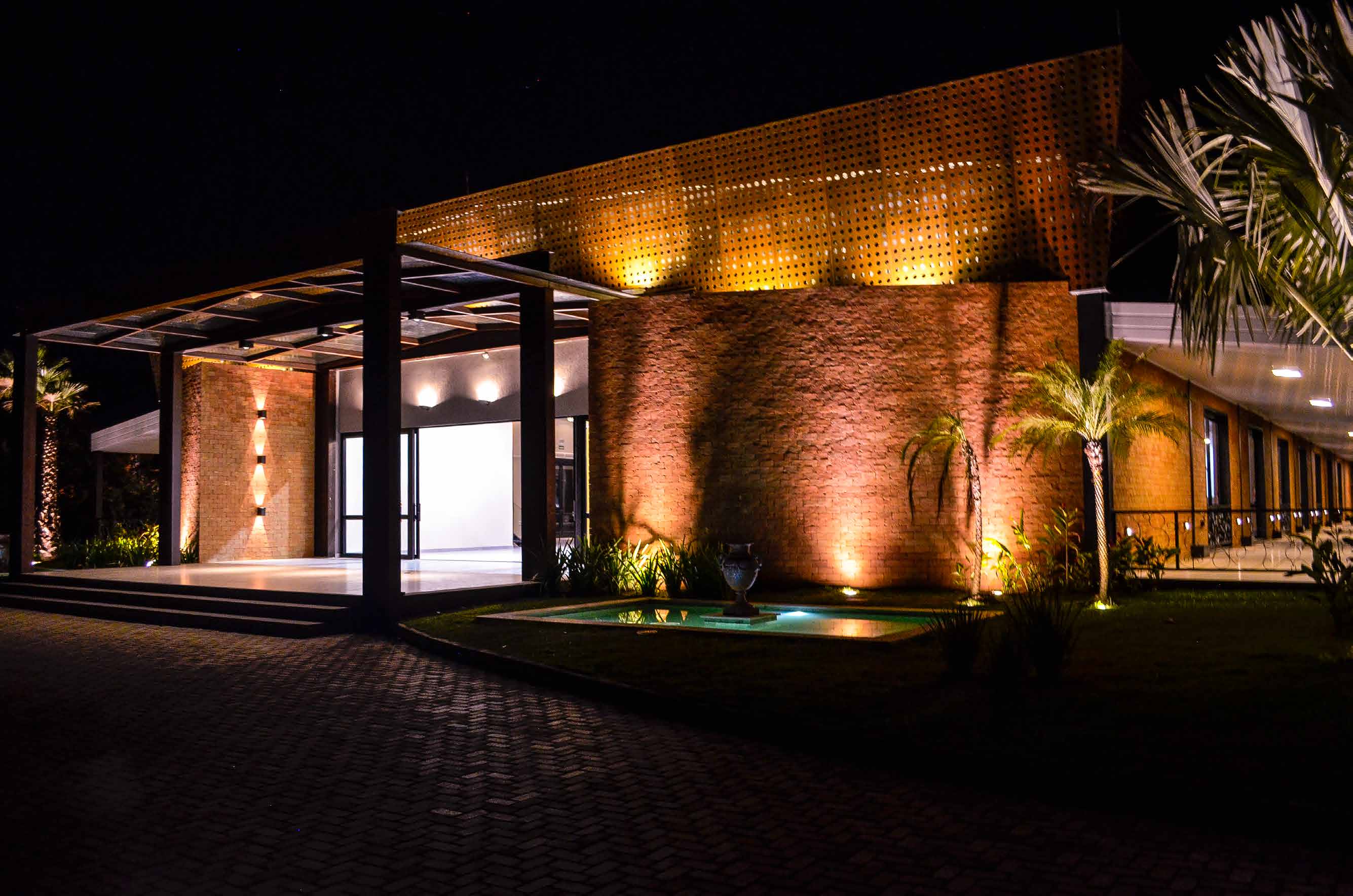 Fachada do Galpon iluminada à noite, em tijolo aparente e aço corten